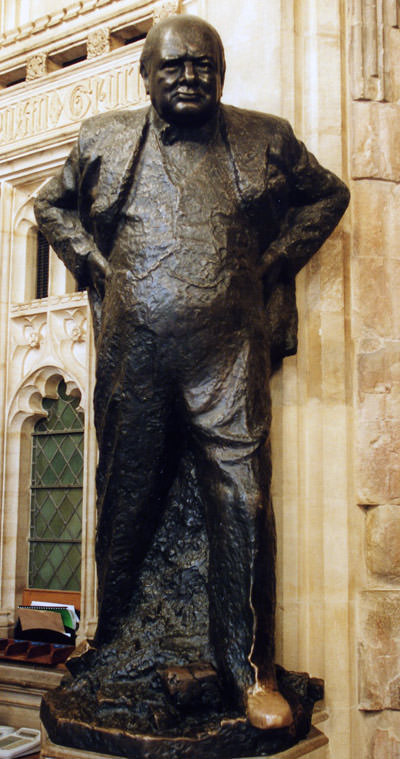 The statue of Winstion Churchill in the House of Commons, his left foot changing to golden color due to superstitious rubbing for good luck; photo by UK Parliament.