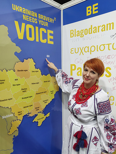 Marina Antonyuk, the director of Ukrainian Incentives, and president of the Association of incoming tour operators of Ukraine, standing in a traditional costume at Place2Go tourism fair in Zagreb, and pointing with a finger on the map of Europe, where Russia, the country that occupied parts of Ukrainian territory, is labeled by a number 404, error code in digital world; photo by Ivan Kralj.