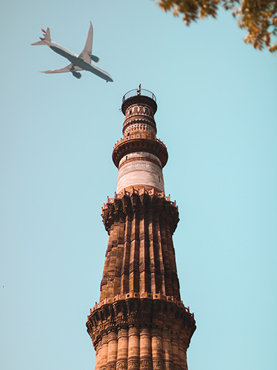 Plane flying over Qutub Minar minaret in New Delhi, India. Every flight is a major contributor to carbon emissions; photo by Akshay Srivastava, Unsplash.