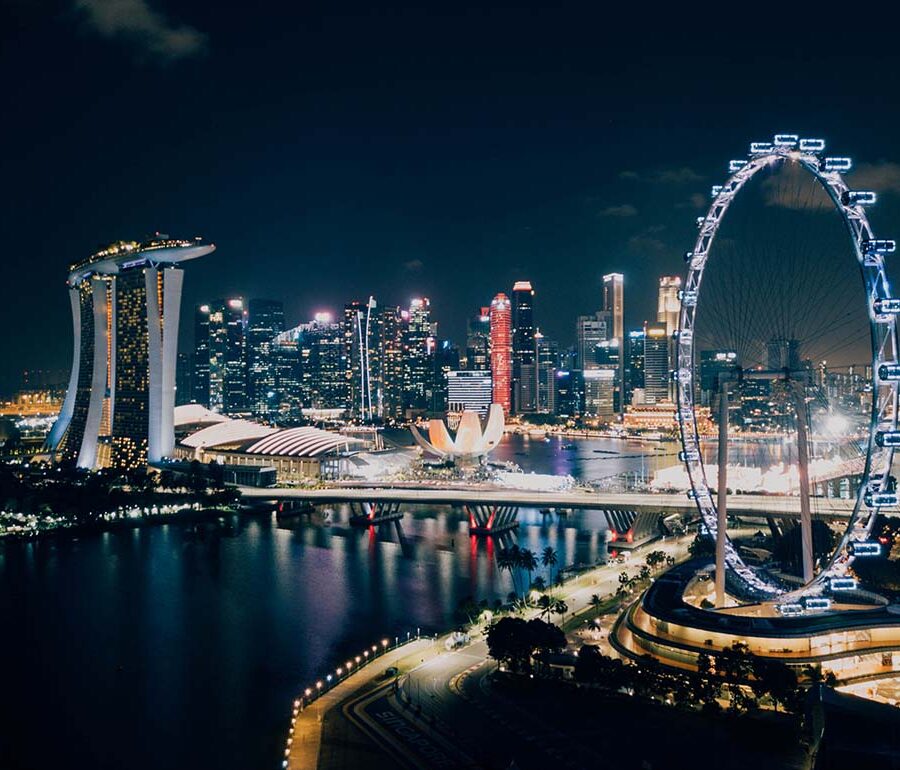 Panorama of Singapore skyline by night, with lighted Singapore Flyer, one of the biggest Ferris wheels in the world, in the foreground; photo by Chuttersnap, Unsplash.