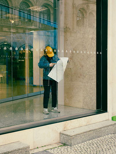 Tourist with a map trapped inside of a building, behind a glass wall; photo by Burcin Ergunt, Unsplash.