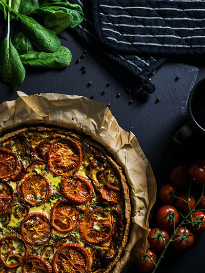 Crusty vegetarian pizza displayed next to basil and cherry tomatos, embracing vegan diet is one of the best ways to reduce carbon footprint; photo by Lum3N, Unsplash.