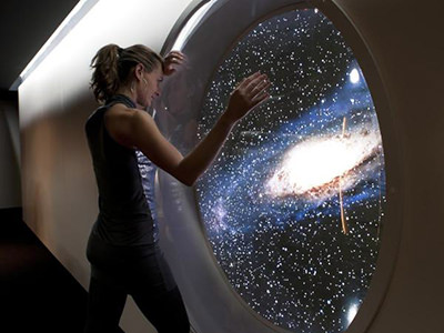 Woman standing next to a round window looking at a galaxy, at Barcelo Sants, space-themed hotel in Barcelona, Spain; photo by Booking.com.