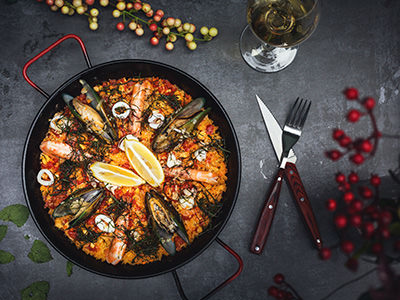 Seafood paella shot from above, with utensils and a glass of wine on the side; photo by Ting Tian, Unsplash.