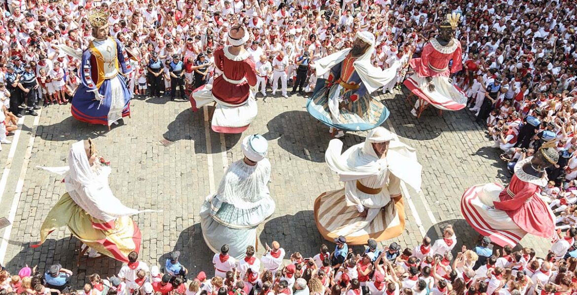 Giant puppets dancing on a street in Spain, surrounded by a lot of spectators; photo by San Fermin Pamplona - Navarra, Unsplash.