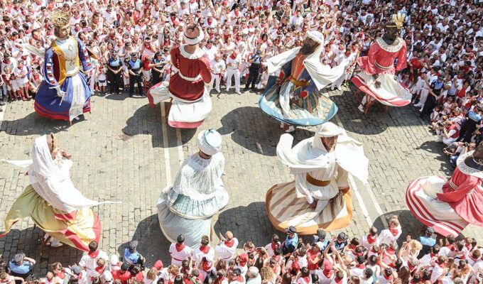 Giant puppets dancing on a street in Spain, surrounded by a lot of spectators; photo by San Fermin Pamplona - Navarra, Unsplash.