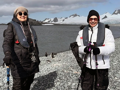Ellie Hamby and Sandy Hazelip, aka TikTok Traveling Grannies, posing in Antarctica on a beach with penguins.