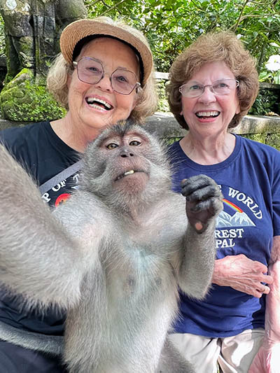 Ellie Hamby and Sandy Hazelip, TikTok Traveling Grannies on a trip around the world at age 80, taking a selfie with a monkey in the foreground.