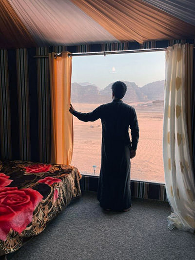 Man looking outside the large windows of a tent in Wadi Rum Star Wars Camp, at desert landscapes of Jordan; photo by Booking.com.