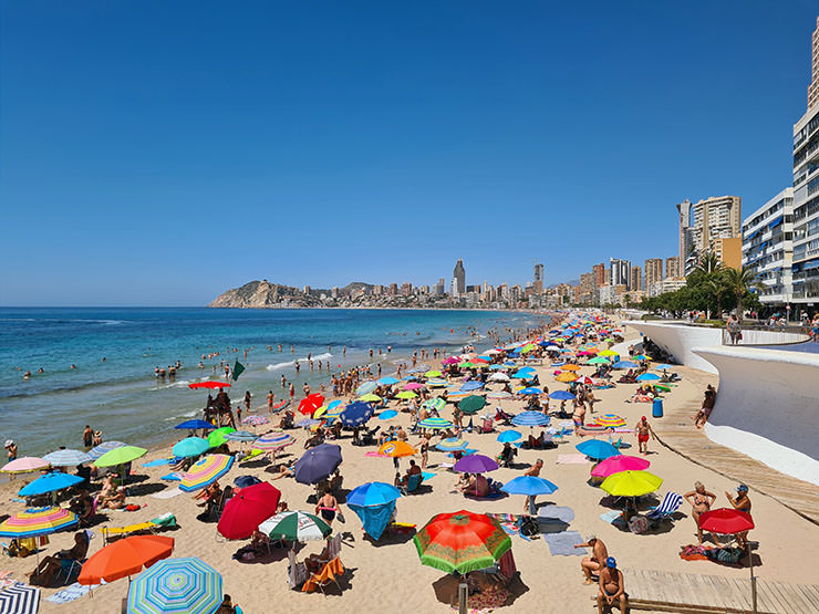 A beach with colorful parasols in Alicante, Spain; photo by Martijn Vonk, Unsplash.