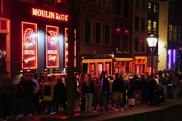 People enjoying their night by the canals of the Red Light District in Amsterdam, Netherlands, one of the cities having issues with overtourism; photo by Gio, Unsplash.