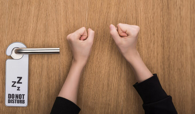 Hands knocking at the hotel door despite the 'Do Not Disturb' sign; photo by Vadim Vasenin, Depositphotos.