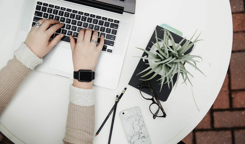 Person working on a laptop next to aloe vera plant, top view; blogxiety or blogging anxiety is experienced by 2 out of 3 bloggers; photo by Corinne Kutz, Unsplash.