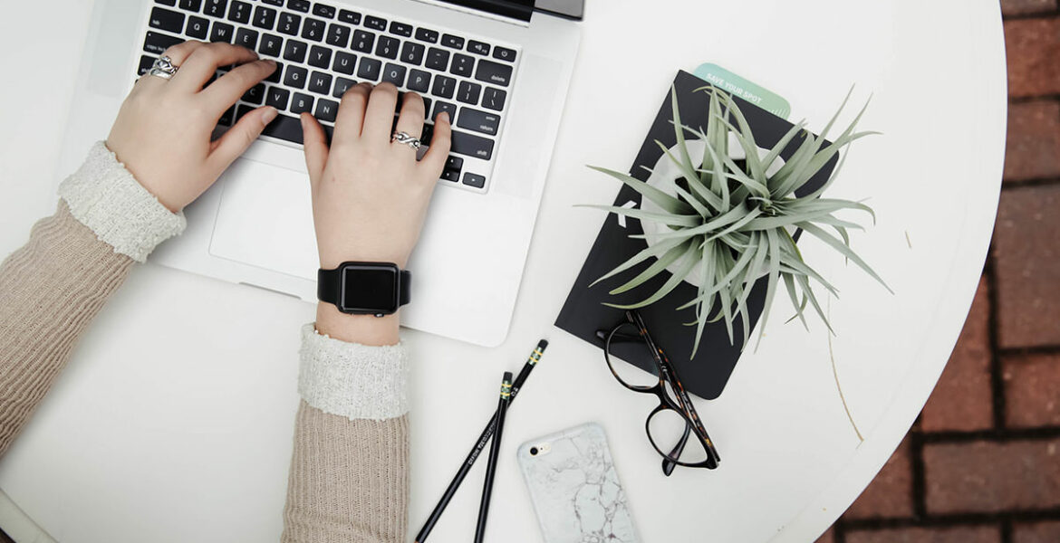 Person working on a laptop next to aloe vera plant, top view; blogxiety or blogging anxiety is experienced by 2 out of 3 bloggers; photo by Corinne Kutz, Unsplash.