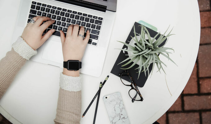 Person working on a laptop next to aloe vera plant, top view; blogxiety or blogging anxiety is experienced by 2 out of 3 bloggers; photo by Corinne Kutz, Unsplash.