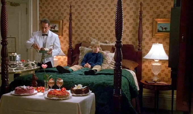 Screenshot of the scene from the movie "Home Alone 2: Lost in New York" where Kevin McCallister sits on the table during the room service of delicacies by the butler; credit 20th Century Fox.