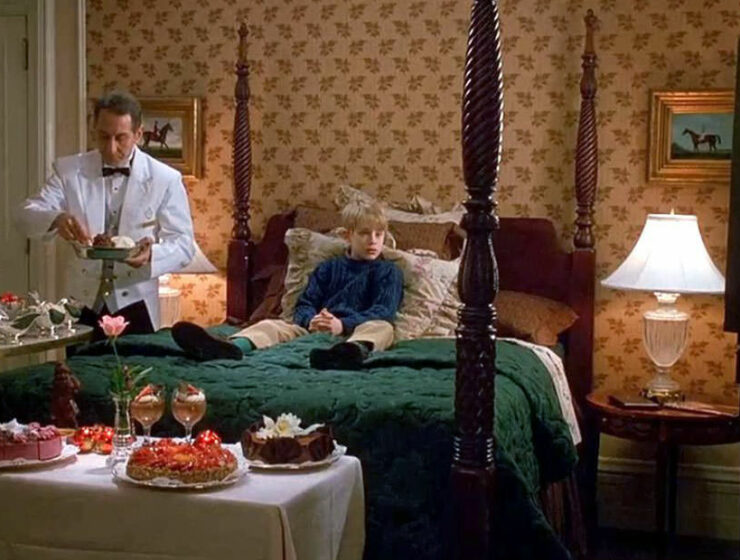 Screenshot of the scene from the movie "Home Alone 2: Lost in New York" where Kevin McCallister sits on the table during the room service of delicacies by the butler; credit 20th Century Fox.