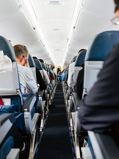 The view of plane aisle while passengers sit in their seats; photo by Hanson Lu, Unsplash.