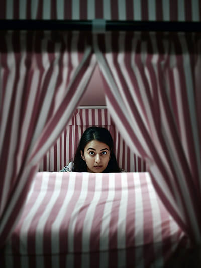 Surprised young woman behind the privacy curtains in a hostel in Delhi; image by Ivan Kralj, Midjourney.