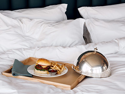Burger with fries on a wooden tray displayed on hotel bed, the most common room service item according to Hotels.com survey; photo by Ryan Neeven.