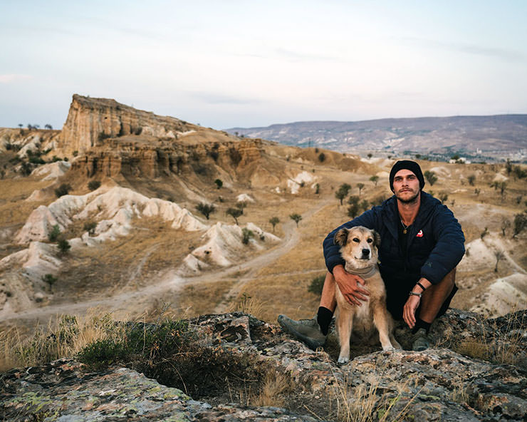 Tom Turcich posing for a picture with his dog Savannah in front of mountainous landscape during their walk around the world.