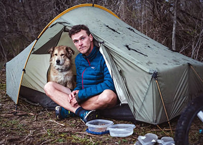 Savannah, the dog, and her owner Tom Turcich, the world walker, sitting in a tent during their adventure.