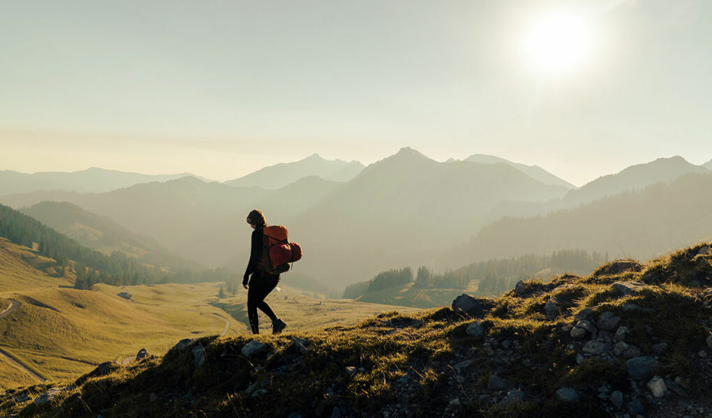 Backpacker walking in the misty mountainous landscape of the green Bernese Highlands, Swiss Alps; photo by Janis Fasel, Unsplash.