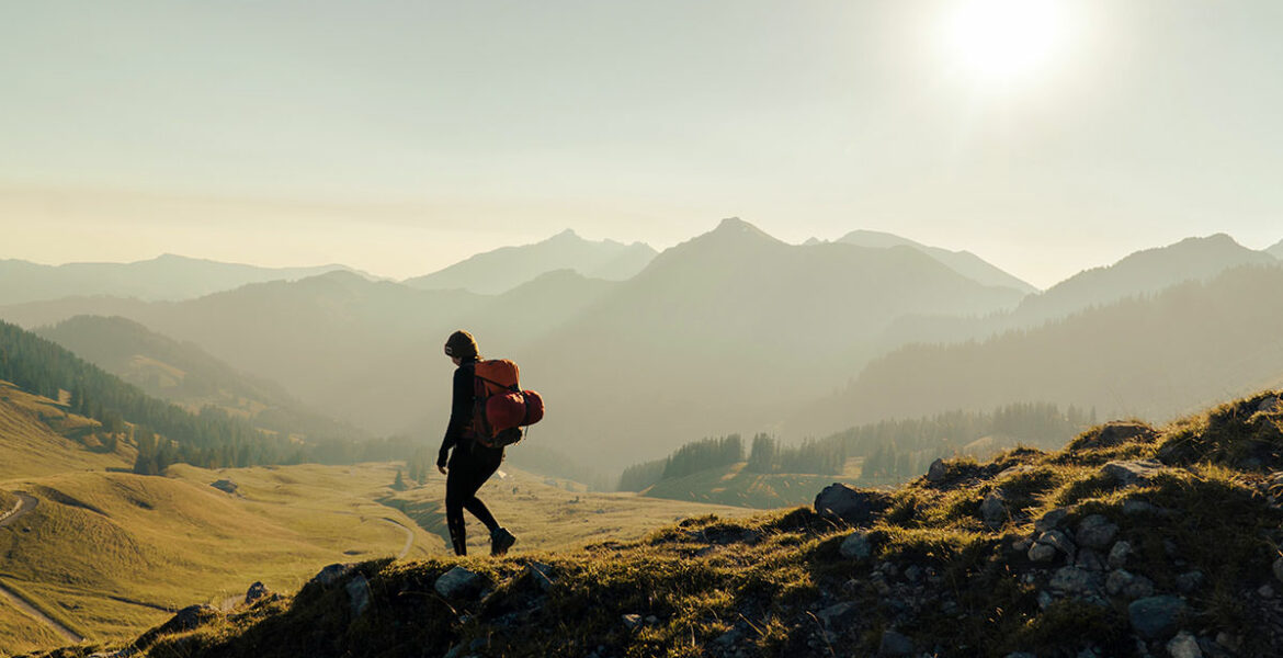 Backpacker walking in the misty mountainous landscape of the green Bernese Highlands, Swiss Alps; photo by Janis Fasel, Unsplash.