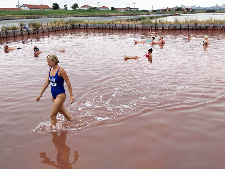 Woman walking through one of Burgas Salt Pans in a swimsuit saying "Beach please", the water is pink because of the microbes thriving in these salt-saturated waters on Bulgarian coastline; photo by Ivan Kralj.