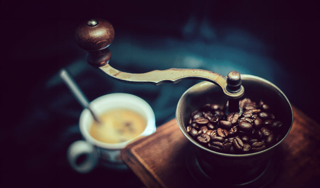 Vintage coffee grinder with a coffee cup in a blurred background - what are the best coffee destinations in the world?; photo by Tom Swinnen, Pexels.