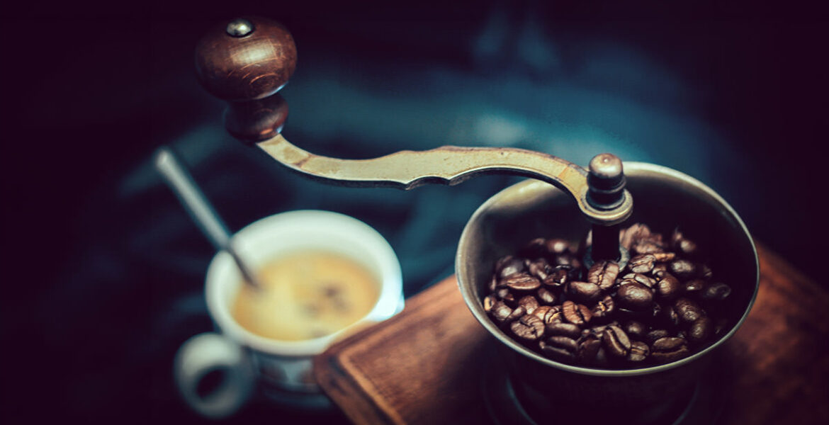 Vintage coffee grinder with a coffee cup in a blurred background - what are the best coffee destinations in the world?; photo by Tom Swinnen, Pexels.