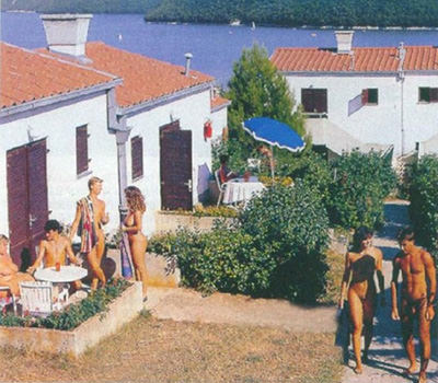 Vintage photograph of Koversada, the first naturist resort established in Istria, Croatia, in 1961, showing young naked people hanging out in front of holiday homes.