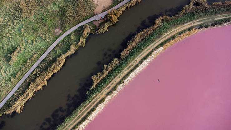 The aerial view of brown-water canal passing by the pink lakes - Lac Rose d'Aigues-Mortes in France; photo by Nathan Cima.