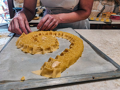 Baker Ružica Ribarić lacing strips of dough around her Rab cake filling, forming distinctive ruffled wrap of the spirally-shaped rapska torta at Kuća rabske torte in Rab, Croatia; photo by Ivan Kralj.