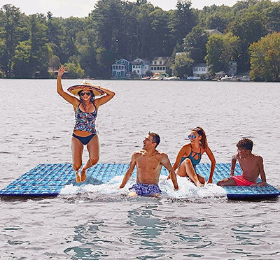 People having fun jumping into the lake from a supersized floating water mat by Aqua, one of the summer must-haves of 2023 on Amazon.