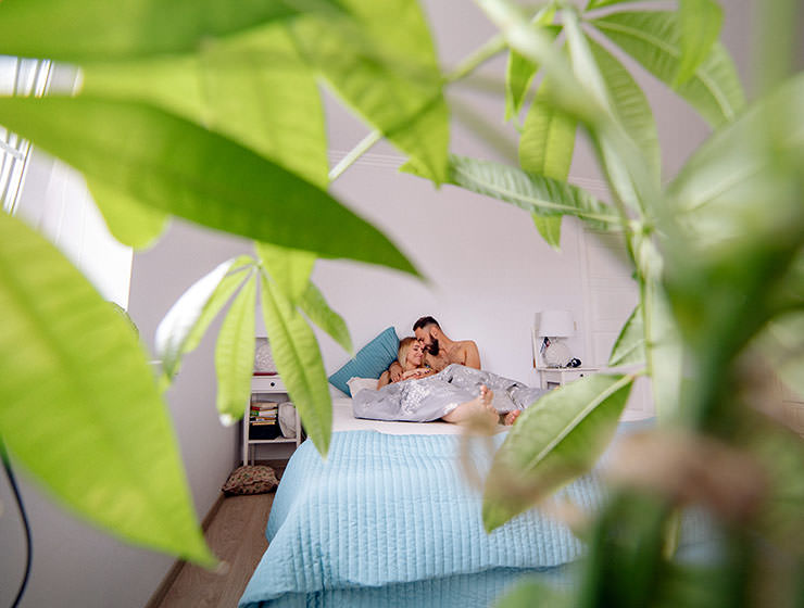 A couple lying in their bed in vacation rental while being filmed by a hidden camera, concealed behind a plant; photo by Yan Krukau, Pexels.