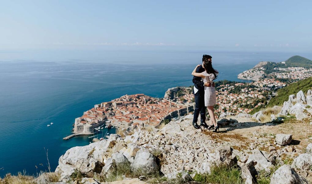 A couple on a honeymoon in Croatia, hugging with the panorama of Dubrovnik in the background; photo by Shevtsovy, Depositphotos.