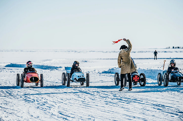Man signaling the start of the race in mini-carts, by waving a red bra in the air, in the snowy landscape of the frozen Lake Baikal, during the MadWay Rally.