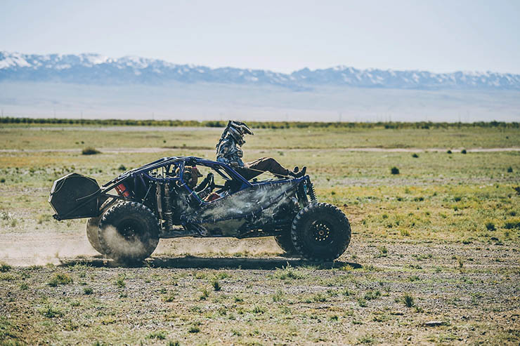 Person with a helmet riding on the top of the Mad Max-style car in the plain of Mongolia, during the MadWay Rally.