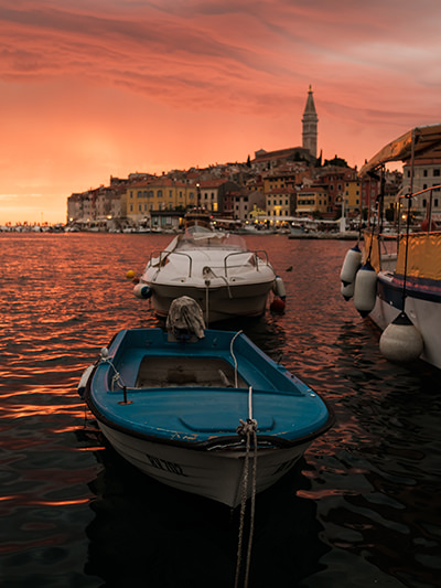Boats in the harbor with Rovinj peninsula under sunset in the background, one of the most romantic towns in Istria and popular honeymoon destination of Croatia; photo by Florin Beudean, Unsplash.