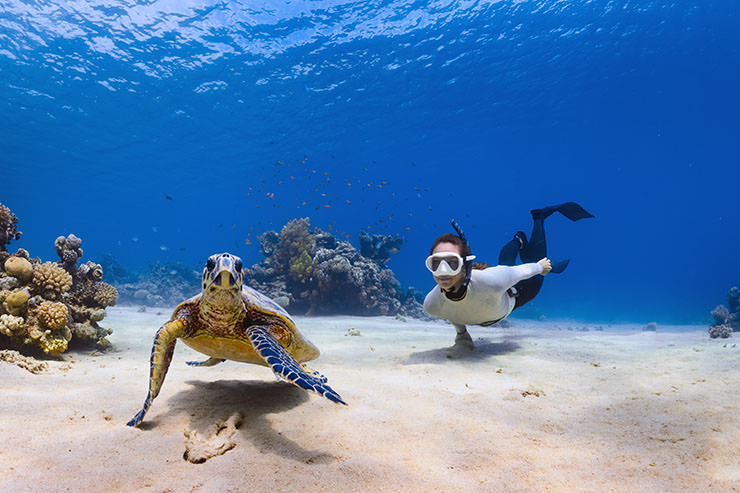 Snorkeler diving undersea in Saudi Arabia, with a turtle swimming in the foreground; photo by Neom, Unsplash.