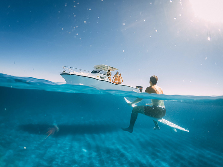 Over-under shot in the style of split-level photography showing a boat and a surfer above and under water; photo by Louilem, GDome.