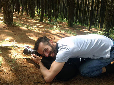 Travel blogger Ivan Kralj kneeling on the forest floor in Bukit Moko, Indonesia, and laughing while trying to photograph a fern dancing in the wind; photo by Fathin Naufal.