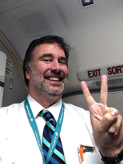Smiling WestJet flight attendant Michael McAdam posing for the camera in the plane, making V-sign with his fingers; McAdam went viral on YouTube for his amusing safety demo presentations; private album.