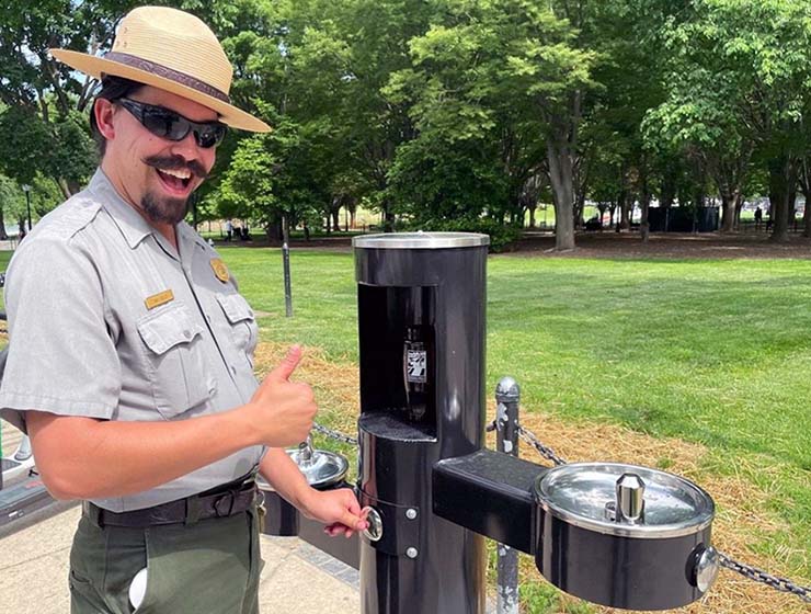 National Park Service ranger giving thumb up with a smiling face, while standing next to a water fountain and promoting hydration.