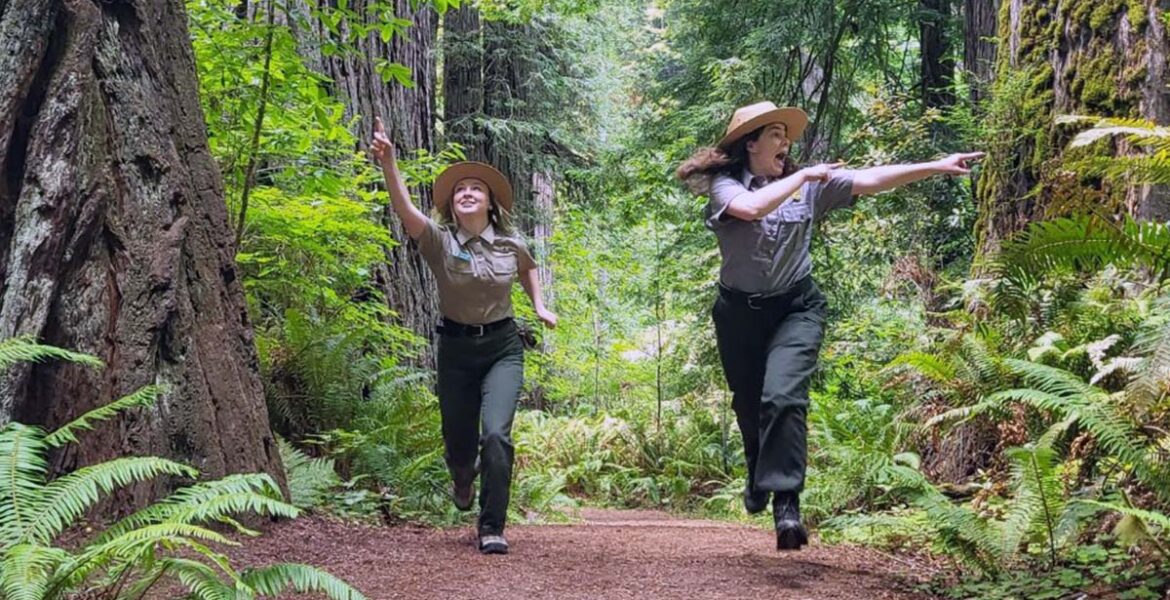 Two female rangers of National Park Service comically pointing at the forest while running through it; NPS humor safety marketing on Twitter.