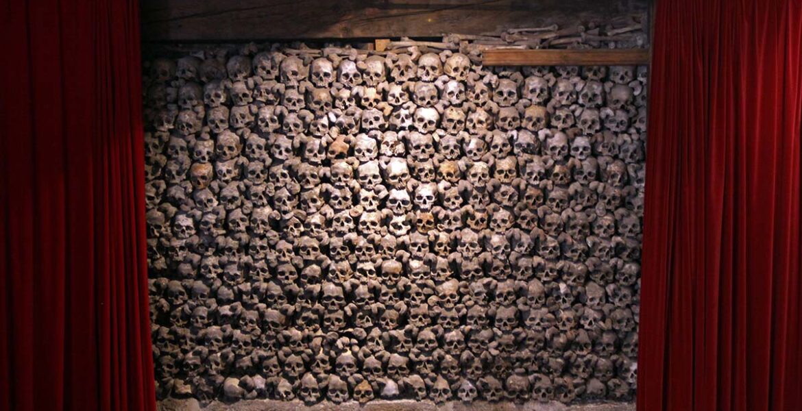 Skull wall framed between two red curtains, like in a theatre, in Beinhaus Leuk, a charnel house in Wallis, Switzerland; photo by Ivan Kralj.