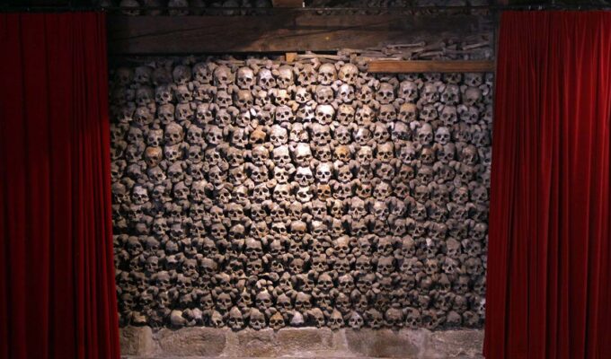 Skull wall framed between two red curtains, like in a theatre, in Beinhaus Leuk, a charnel house in Wallis, Switzerland; photo by Ivan Kralj.