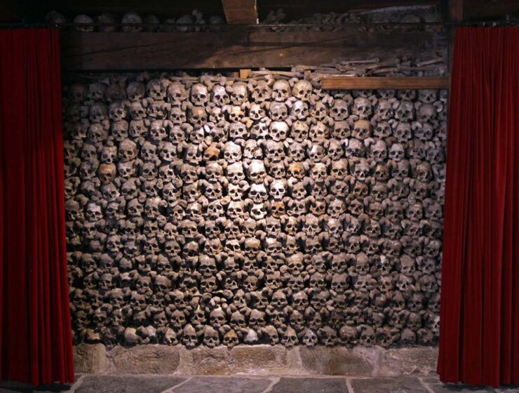 Skull wall framed between two red curtains, like in a theatre, in Beinhaus Leuk, a charnel house in Wallis, Switzerland; photo by Ivan Kralj.