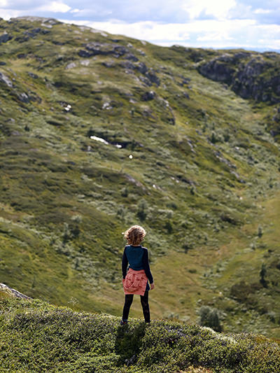 A girl standing on the green hillside in Norway, embracing friluftsliv or outdoor lifestyle; photo by Juliane Liebermann, Unsplash.